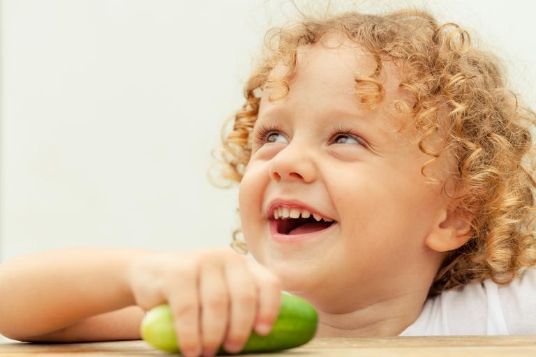 A child holding a small cucumber.